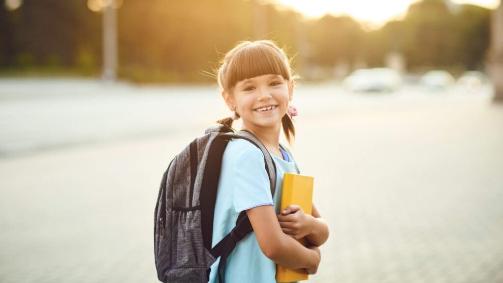 Young child with a backpack holding a book before the first day of child care.