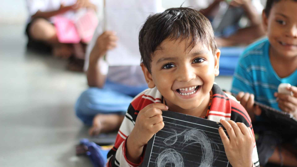 Smiling child holding a drawing during a classroom activity with other children.